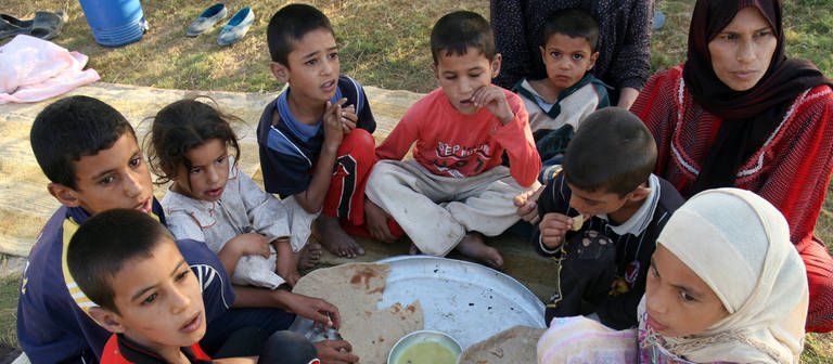 Kinder sitzen im Kreis und essen Brot - Der Alltag der Menschen im Irak ist geprägt von Leid und Krieg.  (Foto: IMAGO, IMAGO / UPI Photo)