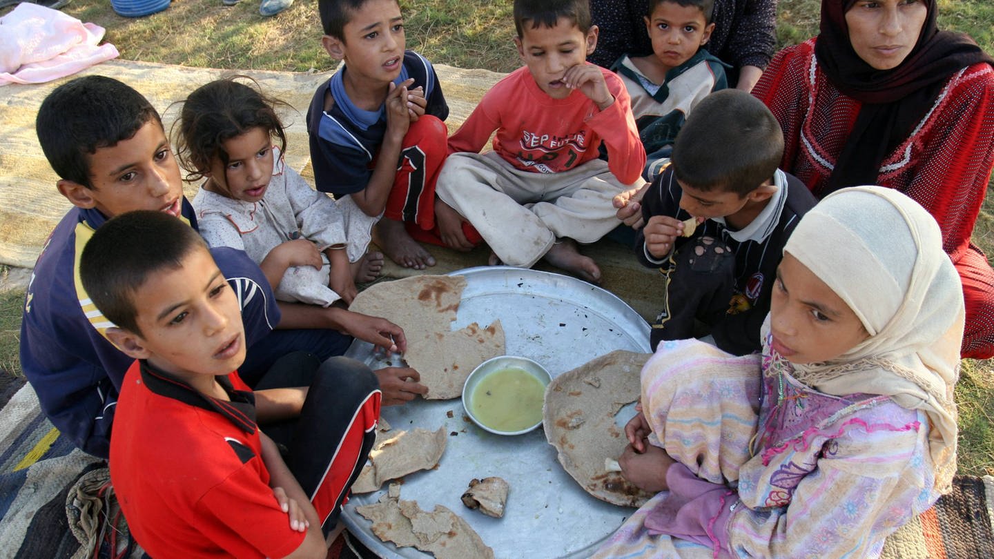 Kinder sitzen im Kreis und essen Brot - Der Alltag der Menschen im Irak ist geprägt von Leid und Krieg. (Foto: IMAGO, IMAGO / UPI Photo)