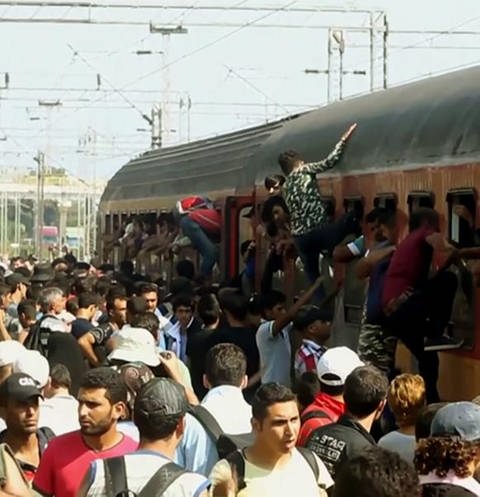 Viele Flüchtlinge stehen an einem Bahnsteig und versuchen in einen überfüllten Zug zu steigen