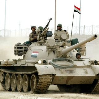 Ein Panzer fährt durch eine staubige Straße in Bagdad, zwei Soldaten schauen hinaus. Internationale Krisen.