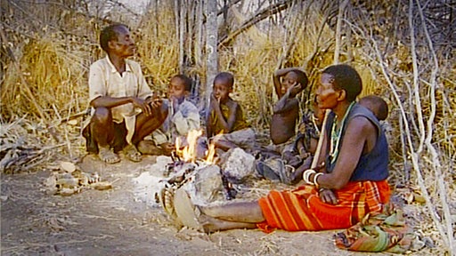 Hadzabe sitzen bei Nacht um ein Lagerfeuer im Dornbusch