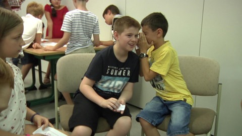 Zwei Jungen sitzen auf Stühlen und flüstern