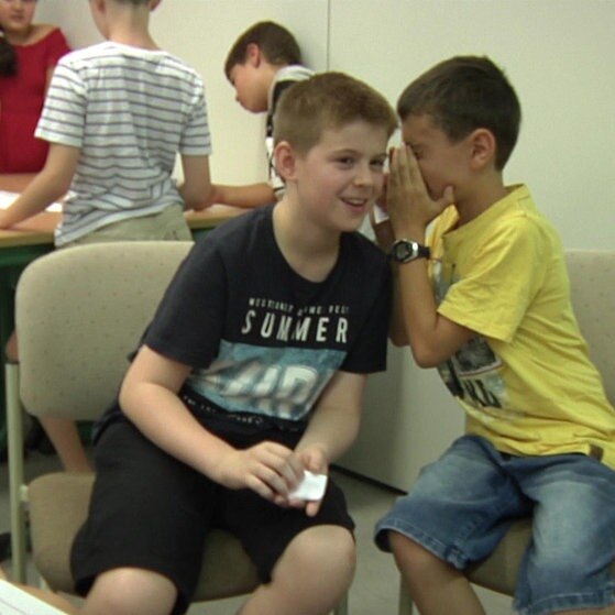 Zwei Jungen sitzen auf Stühlen und flüstern