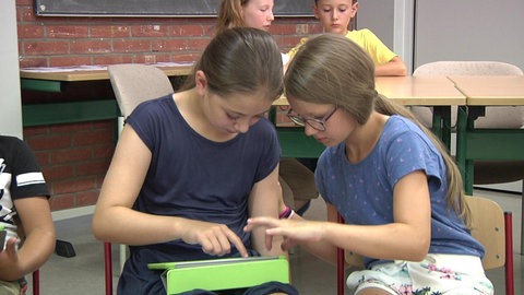Zwei Mädchen sitzen in Klassenraum und nutzen gemeinsam ein Tablet