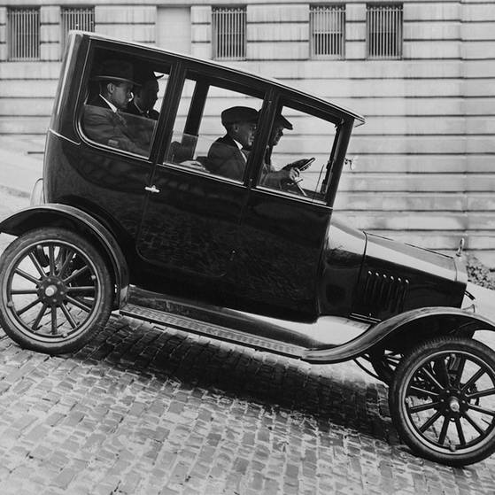 Ford-Modell T21, ein schwarz-weiß Foto eines altmodischen Autos, das eine steile Straße runterfährt.