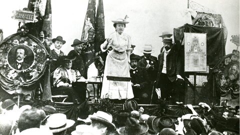Rosa Luxemburg, die auf einer Bühne steht und redet.
