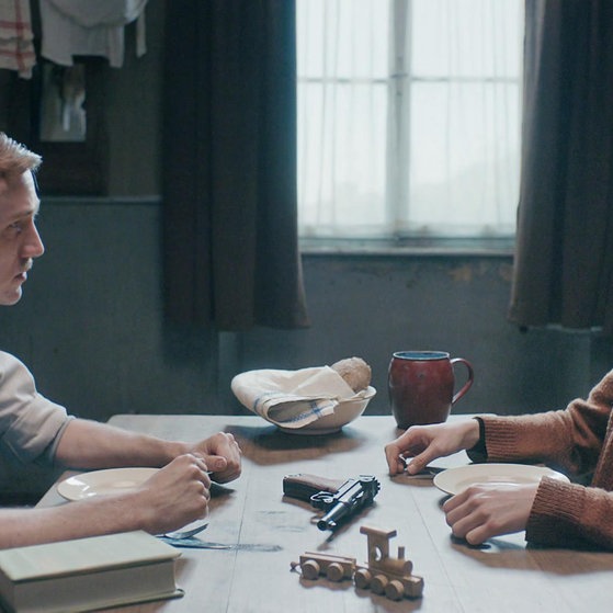 Spielszene: Hans und Magdalena Beimler am Esstisch, zwischen sich eine Waffe.