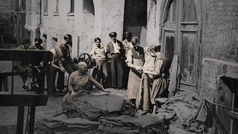 Historische Aufnahme: Männer und Frauen in ärmlich wirkendem Hinterhof.