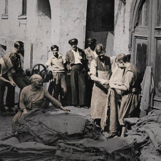 Historische Aufnahme: Männer und Frauen in ärmlich wirkendem Hinterhof.