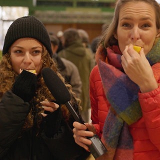 Stefanie und eine Markthändlerin beißen in Zitronenstücke in der Markthalle von Joigny. Welche französischen Begriffe gibt es rund um das Gemüse- und Obstangebot?