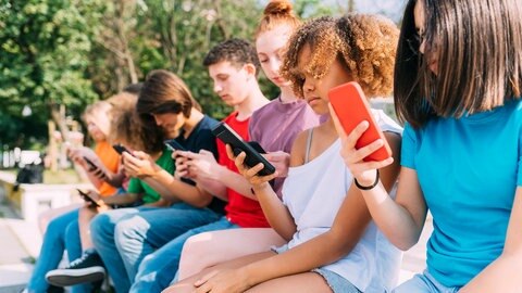 Junge Menschen sitzen in einer Reihe und schauen jeweils aufs Smartphone.