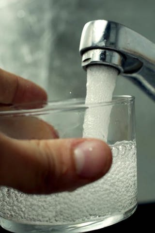 Ein Glas wird aus einem Wasserhahn befüllt
