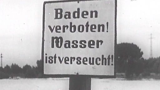 Ein schwarz-weiß Bild eines Schildes auf dem steht: "Baden verboten! Wasser ist verseucht!"