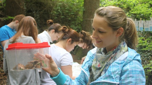 Frau hält Plastikbehälter mit Bodenproben.