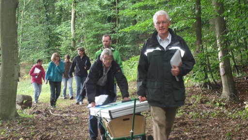 Gruppe Erwachsene mit Bollerwagen im Wald.