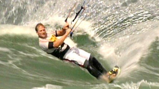 Ein schwarz-weiß gekleideter Surfer auf einer großen Welle. (Foto: SWR – Screenshot aus der Sendung)