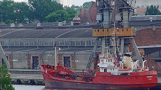 Ein rot gestrichenes Schiff vor einem alten Hafengebäude. Im Hintergrund sind Industriebauten zu sehen. (Foto: www.sxc.hu)