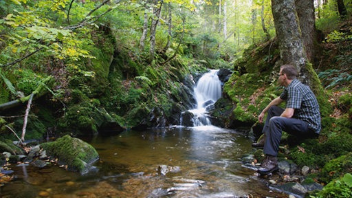 Ein Mann sitzt an einem Bach.