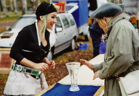 Mona (links) auf dem Flohmarkt. Eine ältere Frau interessiert sich für Monas Vase. (Foto: SWR / Ireen Hillmann)