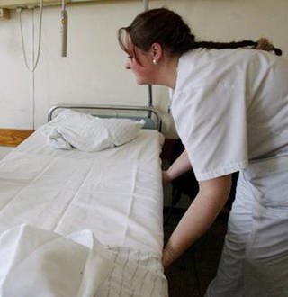 Eine Pflegerin macht ein Krankenhausbett (Foto: picture-alliance / dpa)