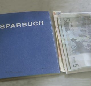 Ein blaues Sparbuch und mehrere Geldscheine nebeneinander