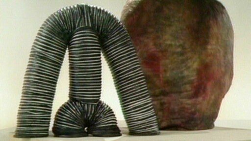 Eine Röhrenfigur steht neben einem Klumpen.