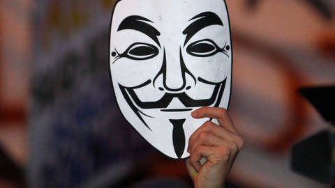 Eine Hand hält eine Maske mit Guy Fawkes-Gesicht hoch