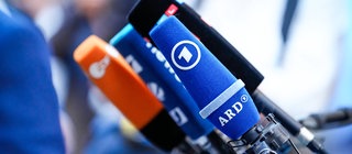 Mehrere Mikrofone von verschiedenen Medien auf einem Tisch. Wie werden Nachrichten gemacht? Warum sind Nachrichten wichtig?