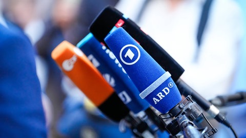 Mehrere Mikrofone von verschiedenen Medien auf einem Tisch. Wie werden Nachrichten gemacht? Warum sind Nachrichten wichtig?