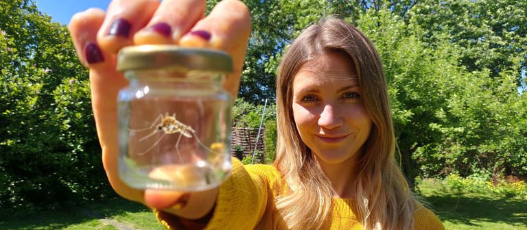 neuneinhalb-Reporterin Jana steht im Garten und zeigt eine Mücke in einem Glas (Foto: WDR, tvision)