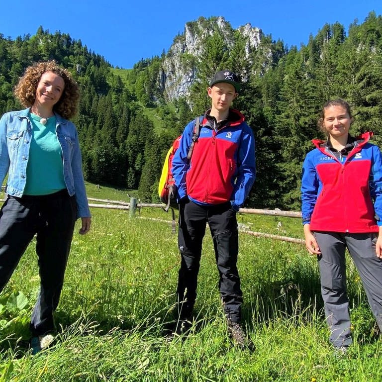 neuneinhalb-Reporterin Gesa, Korbinian und Sophia stehen vor der Bergkulisse der Bayrischen Voralpen. (Foto: WDR, tvision)