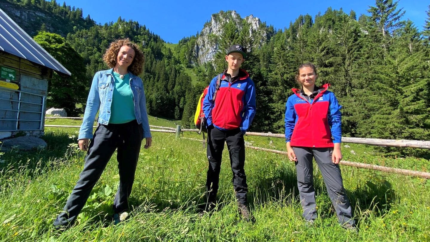 neuneinhalb-Reporterin Gesa, Korbinian und Sophia stehen vor der Bergkulisse der Bayrischen Voralpen. (Foto: WDR, tvision)