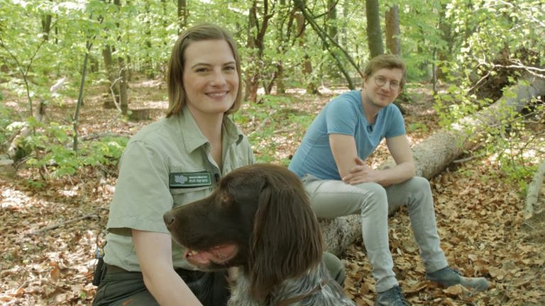 Försterin Andrea Zimmermann, Hund Cuno und neuneinhalb-Reporter Robert sitzen auf einem Baumstamm in Andreas Waldrevier. (Foto: WDR, tvision)