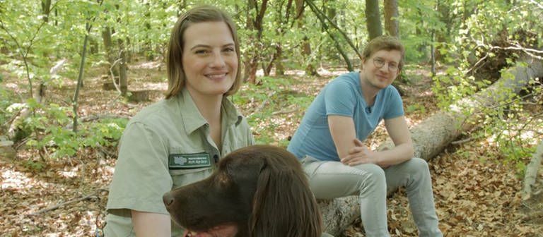 Försterin Andrea Zimmermann, Hund Cuno und neuneinhalb-Reporter Robert sitzen auf einem Baumstamm in Andreas Waldrevier. (Foto: WDR, tvision)