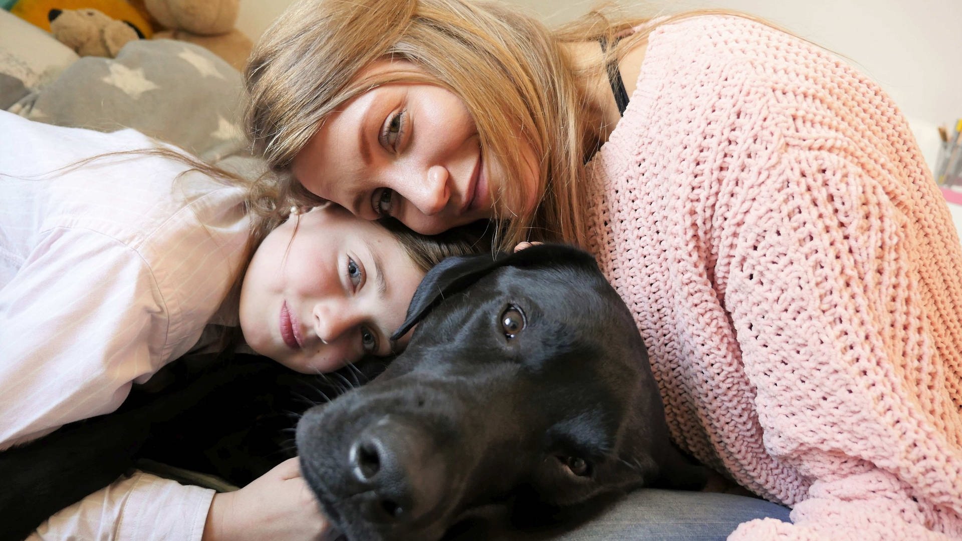 neuneinhalb-Reporterin Jana und Siona kuscheln mit Sionas schwarzem Labrador Pluto. (Foto: WDR, tvision)