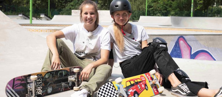 neuneinhalb-Reporterin Jana und Lea sitzen mit ihren Skateboards auf einer Skateboard-Rampe.  (Foto: WDR, tvision)