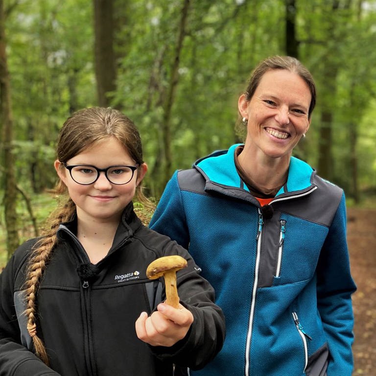 neuneinhalb-Reporter Robert mit Johanna und ihrer Mutter Melanie im Wald. Johanna und Robert halten Pilze in die Kamera. (Foto: WDR, tvision)