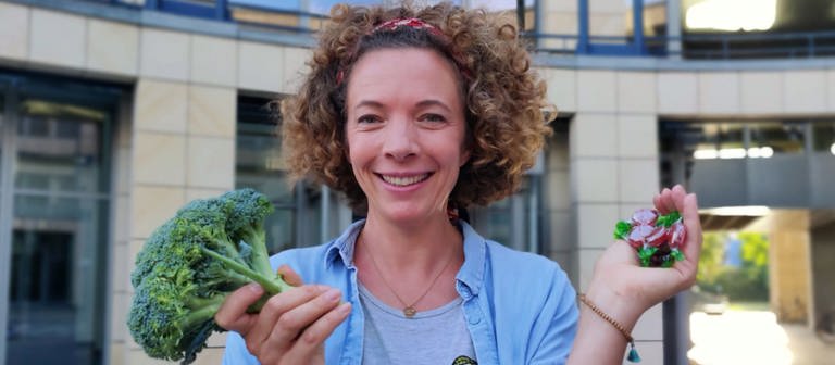 neuneinhalb-Reporterin Gesa hält einen Brokkoli und eine Handvoll Bonbons ins Bild. (Foto: WDR, tvision)