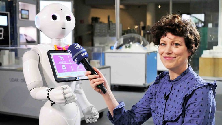 neuneinhalb-Reporterin Malin hält dem humanoiden Roboter 'Pepper' ihr Mikro hin.