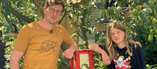 neuneinhalb-Reporter Robert und Jonte (14) stehen vor seinem umgebauten Kaugummiautomaten. Daraus kann man sich nun Samen für Blühwiesen ziehen.