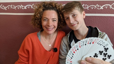 neuneinhalb-Reporterin Gesa zusammen mit Timm, der einen Kartenfächer in der Hand hält