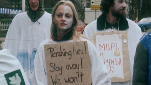 Demonstranten in weißen Gewändern, Frau mit Transparent “Pershing hey! Stay away!” (Foto: SWR - Screenshot aus der Sendung)