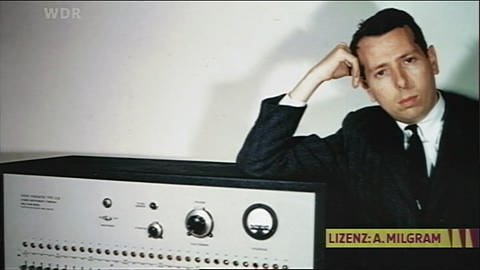 Foto des Psychologen Stanley Milgram, der an einem Messgerät lehnt;