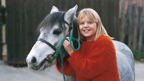 Ein Mädchen steht neben einem grauen Pony.