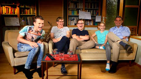 Eltern und drei Kinder sitzen lachend auf dem Sofa im Wohnzimmer. (Foto: SWR/probono)