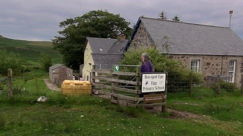 Drei kleine Gebäude in grüner Landschaft.