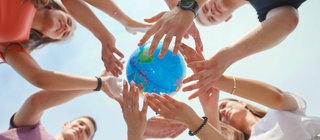 Symbolbild für Sport und Spiele auf der ganzen Welt: Mehrere Personen stehen im Kreis strecken die Arme nach oben und halten gemeinsam einen Globus. Das Bild ist von unten fotografiert. 