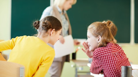 Zwei Schülerinnen sprechen miteinander im Klassenraum: Bei Sprache einfach erklärt gibt es Erklärvideos für den Deutschunterricht.