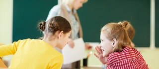 Zwei Schülerinnen sprechen miteinander im Klassenraum: Bei Sprache einfach erklärt gibt es Erklärvideos für den Deutschunterricht.
