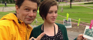 Moderator Andre Gatzke neben dem Mädchen Lily, hinter ihnen hängen Fotos an einer Wäscheleine.